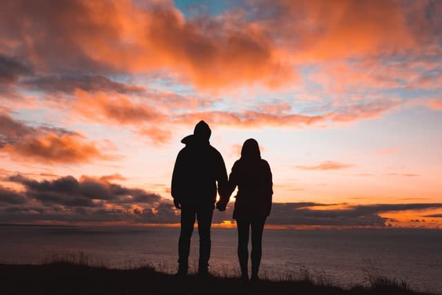Amoureux se tenant la main, regardant le coucher de soleil.